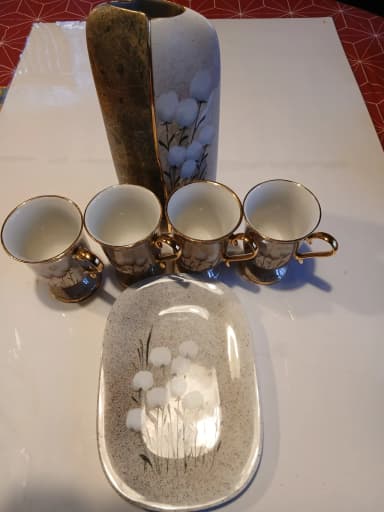 Cuatro tazas de café con borde dorado, jarrón y bandeja con flores