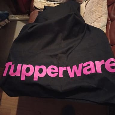 Musta Tupperware-pöytäliina vaaleanpunaisella tekstillä